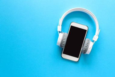 Beyaz kablosuz kulaklık ve mavi arka plan akıllı telefon. Üstten Görünüm. Kopya alanı