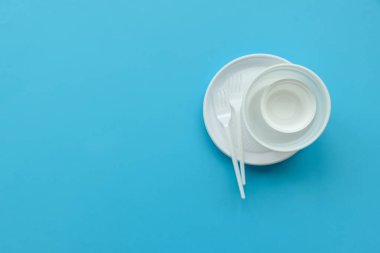 Tek kullanımlık beyaz plastik tabak ve çatal mavi zemin üzerine. Uzay kopyalayın. Üstten Görünüm. Eko ve dünya kavramı kaydetmek.