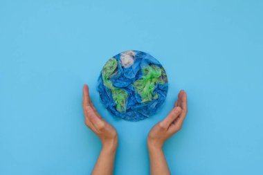 Gezegen holding eller dünya plastik tek kullanımlık paketleri mavi zemin üzerine yapılmıştır. Dünya, yaratıcı, çevre kirliliği veya Dünya Dünya günü kavramı kaydedin. Üstten Görünüm