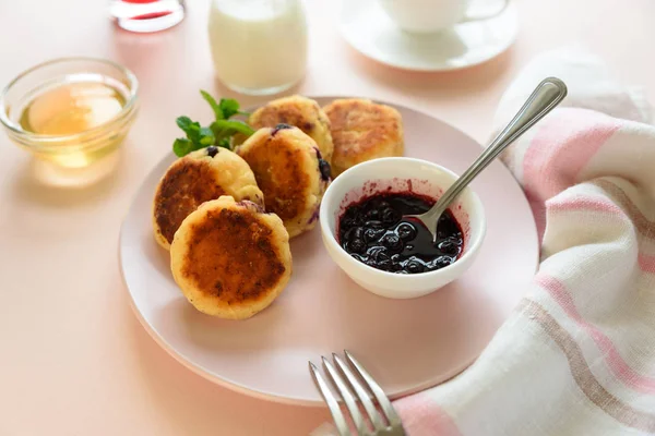 Cottage cheese pancakes with blueberry, honey, jam and coffee. Ukrainian syrniki, cottage cheese fritters or pancakes on pink wooden background. Healthy eating concept. Selective focus