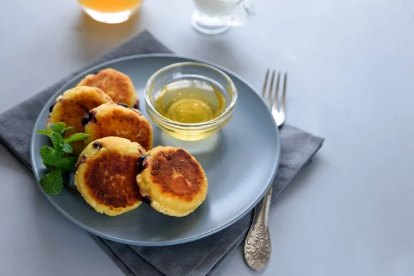 Cottage cheese pancakes with blueberry, honey, jam and coffee. Ukrainian syrniki, cottage cheese fritters or pancakes on gray wooden background. Healthy eating concept. Selective focus