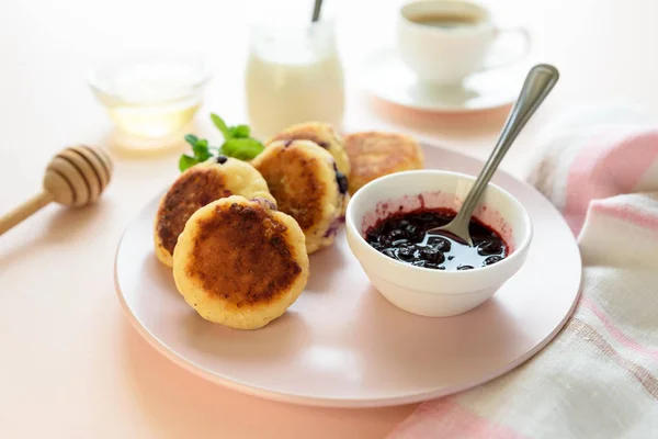 Cottage cheese pancakes with blueberry, honey, jam and coffee. Ukrainian syrniki, cottage cheese fritters or pancakes on pink wooden background. Healthy eating concept. Selective focus