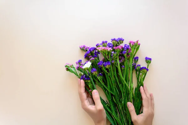 Feminine hands holding bouquet of sea lavender flowers (Limonium) on pink background. Top view. Copy space