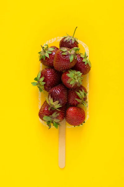Fresh strawberry for ice cream on painted popsicle shape over yellow background. Top view. Copy space. Organic fruit. Food ingredients. Vegetarian, vegan, detox, clean eating concept.