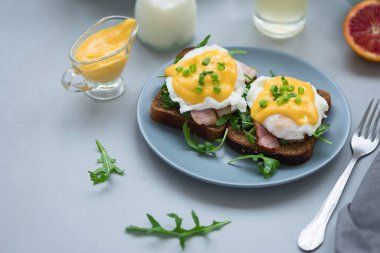 Arugula, pastırma ve gri ahşap arka plan üzerinde hollandaise sos ile yumurta Benedict kapatın. Yumuşak odak. Sağlıklı beslenme konsepti