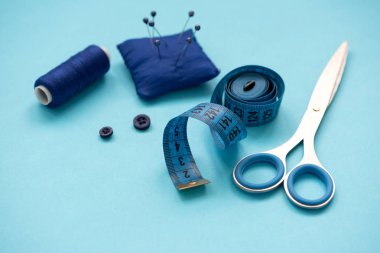 Mavi arka plan üzerinde iplikler, makas, iğne, kumaş, düğmeler ve dikiş bandı ile dikiş aksesuarları. Üst te. Düz yatıyordu.