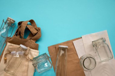 Tekstil eko çanta, kağıt paketleri ve cam kavanoz mavi arka plan üzerinde yatan. Çevre dostu, yeniden kullanım veya sıfır atık konsepti. Üst te. Düz yatıyordu