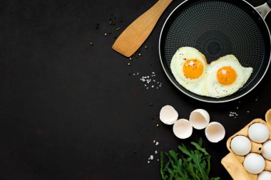 Arugula yaprakları ile tavada kızarmış yumurta, siyah ahşap arka plan üzerinde kahvaltı için tuz ve biber. Üst te. Düz yatıyordu. Kopya alanı. Sağlıklı gıda kavramı