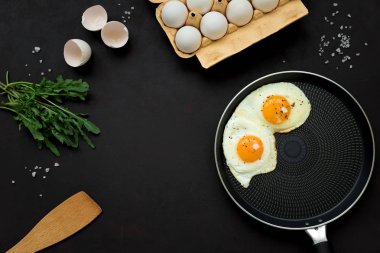 Arugula yaprakları ile tavada kızarmış yumurta, siyah ahşap arka plan üzerinde kahvaltı için tuz ve biber. Üst te. Düz yatıyordu. Kopya alanı. Sağlıklı gıda kavramı