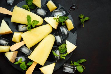 Yuvarlak koyu kayrak plaka üzerinde buz, kavun dilimleri ve nane ile ev yapımı kavun dondurma, pops veya popsicles. Yaz yemeği. Düz yatıyordu. Üstte görüntü