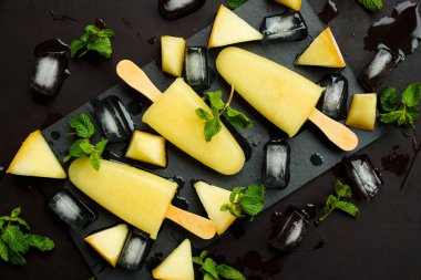 Dikdörtgen koyu kayrak tabakta ev yapımı kavun dondurma, pops veya buzlu dondurma buz, kavun dilimleri ve nane. Yaz yemeği. Düz yatıyordu. Üstte görüntü