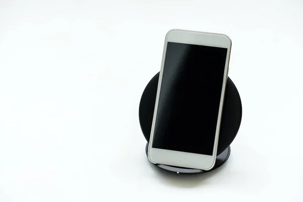 White smartphone charged by wireless charger on white wooden background. Wireless charge or digital technology concept