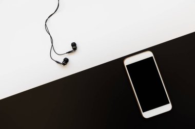 Siyah kulaklıklı, beyaz arka planda beyaz akıllı telefonlu düz bir daire. Kişisel aksesuarların üst görünümü.