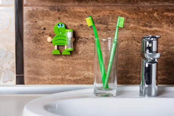 Original and orthodontic toothbrushes in glass and timer on wall — Stock Photo, Image