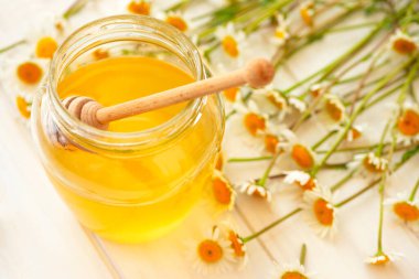 Beyaz ahşap arka planda taze papatya çiçekleri olan bir kavanoz altın bal. Yumuşak odak