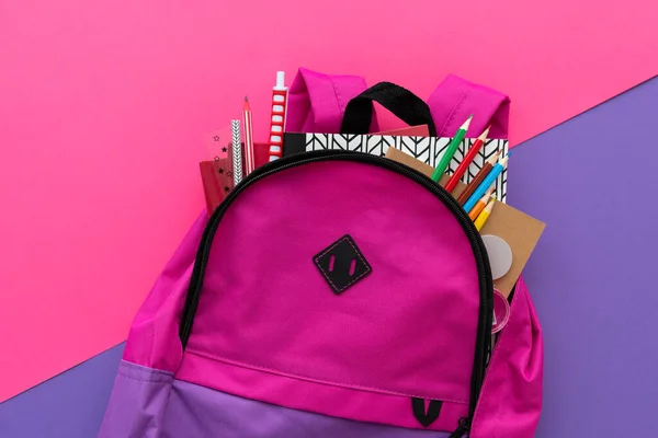 Back to school concept. Backpack with school supplies on purple background. Top view. Copy space