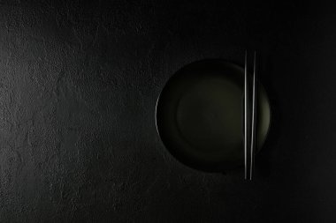 Siyah arka planda yemek çubuğu olan boş seramik tabak. Düz Yat. Üst Manzara. Model