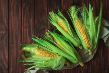 Kahverengi ahşap masadaki koçanlarda taze mısır. Hasat konsepti