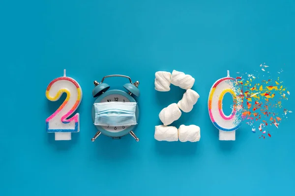 2020 yılında mumlardan, lokum ve çalar saatten yapılmış koruyucu maske takarak mavi arka planda dağılım etkisi yaratıyor. Yeni yıl 2021 kutlaması ya da 2020 yılı sonu konsepti. Üst Manzara. Düz yatıyordu