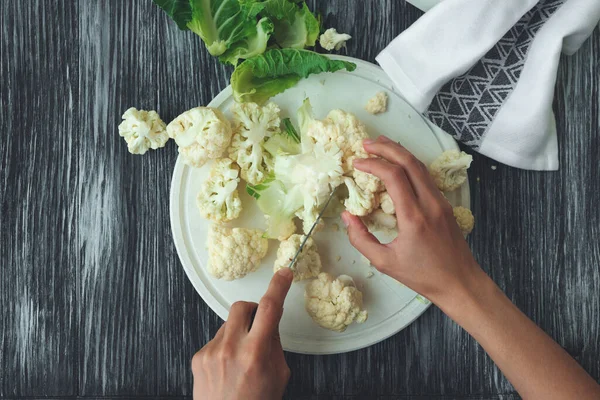 Feminine hands cutting fresh cauliflower on wooden table. Summer food concept. Top view