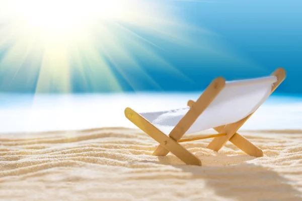 Deck chair on sandy beach with blurry blue ocean and sun beams on sky. Social distancing or COVID-19 protection at summer holidays. Summer background. Soft focus