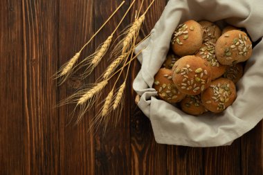 Kahverengi ahşap zemin üzerinde kepek, ayçiçeği ve balkabağı çekirdekli ev yapımı çıtır ekmekli çörek sepeti. Üst görünüm.