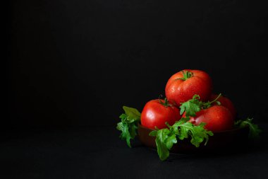 Koyu arkaplanda roka kaplı taze olgun domatesler. Boşluğu kopyala