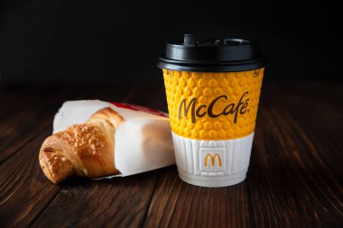 McDonald 's restoranı. Koyu ahşap arka planda kruvasan ile McCafe kağıt kahve. Lviv, Ukrayna - 18 Haziran 2020