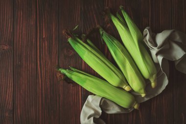 Kahverengi ahşap masadaki koçanlarda taze mısır. Hasat konsepti