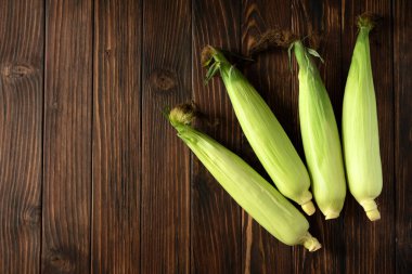 Kahverengi ahşap masadaki koçanlarda taze mısır. Hasat konsepti