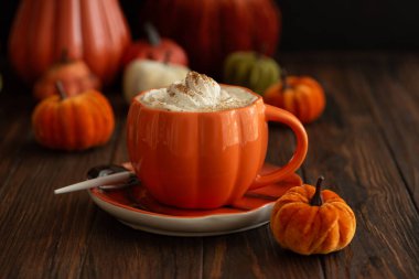 Balkabağı şeklinde bir kupada, sonbahar dekoruyla çevrili, krema ve baharatlı, kabak şeklinde bir latte.