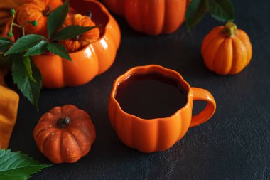 Balkabağı şekilli çaydanlık ve fincanla sonbahar çay seti ve siyah ahşap bir masada dekoratif balkabakları..