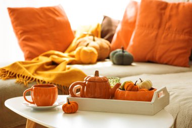 Balkabağı, çaydanlık, çay fincanı ve rahat battaniyeli sonbahar oturma odası dekoru..