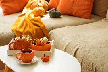 Balkabağı, çaydanlık, çay fincanı ve rahat battaniyeli sonbahar oturma odası dekoru..