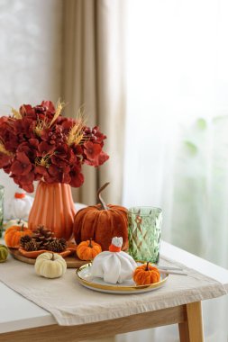 Süslü balkabakları, mumlar ve beyaz ahşap masa üzerindeki iplik ışıkları ile Şükran Günü sofrası.