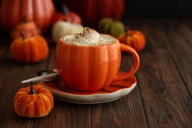 Balkabağı şeklinde bir kupada, sonbahar dekoruyla çevrili, krema ve baharatlı, kabak şeklinde bir latte.