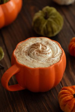 Balkabağı şeklinde bir kupada, sonbahar dekoruyla çevrili, krema ve baharatlı, kabak şeklinde bir latte.