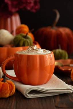 Balkabağı şeklinde bir kupada, sonbahar dekoruyla çevrili, krema ve baharatlı, kabak şeklinde bir latte..