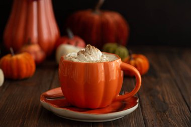 Balkabağı şeklinde bir kupada, sonbahar dekoruyla çevrili, krema ve baharatlı, kabak şeklinde bir latte.