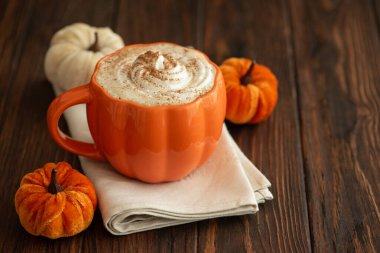 Balkabağı şeklinde bir kupada, sonbahar dekoruyla çevrili, krema ve baharatlı, kabak şeklinde bir latte.