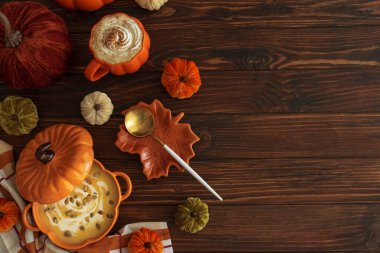 Balkabağı şeklindeki bir kâsede balkabağı çorbası, balkabağı latte, kızarmış ekmek ve koyu ahşap masada şenlikli bir dekor ile sonbahar yemeği. Üst Manzara. Boşluğu kopyala