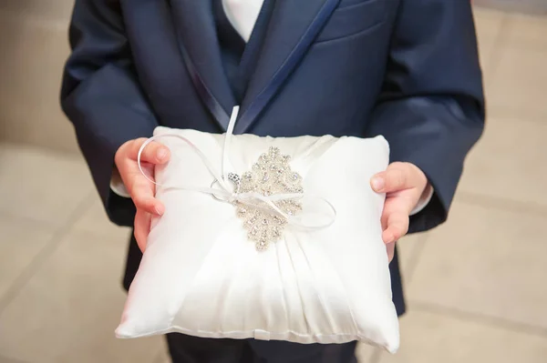 A close up view of a ring bearer holding a bridal wedding pillow decorated with sequins and the bride`s ring.