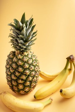 Olgun bir ananas ve sarı bir arka plan üzerinde dört sarı muz.