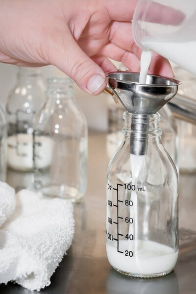 A man pours milk through a silver funnel into a small glass jar.