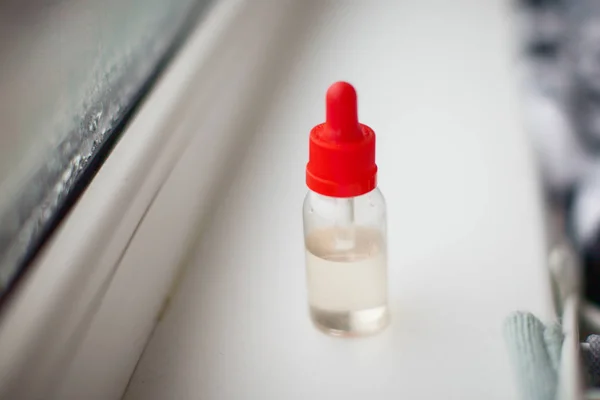 Transparent bottle with red cover on the window sill. Some liquid in the transparent bottle.