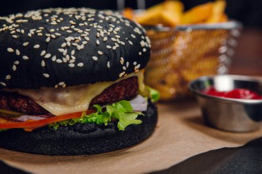 Lokantada masada patates kızartması ve ketçap ile siyah hamburger. Fast food, abur cubur