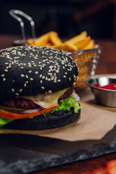 Lokantada masada patates kızartması ve ketçap ile siyah hamburger. Fast food, abur cubur