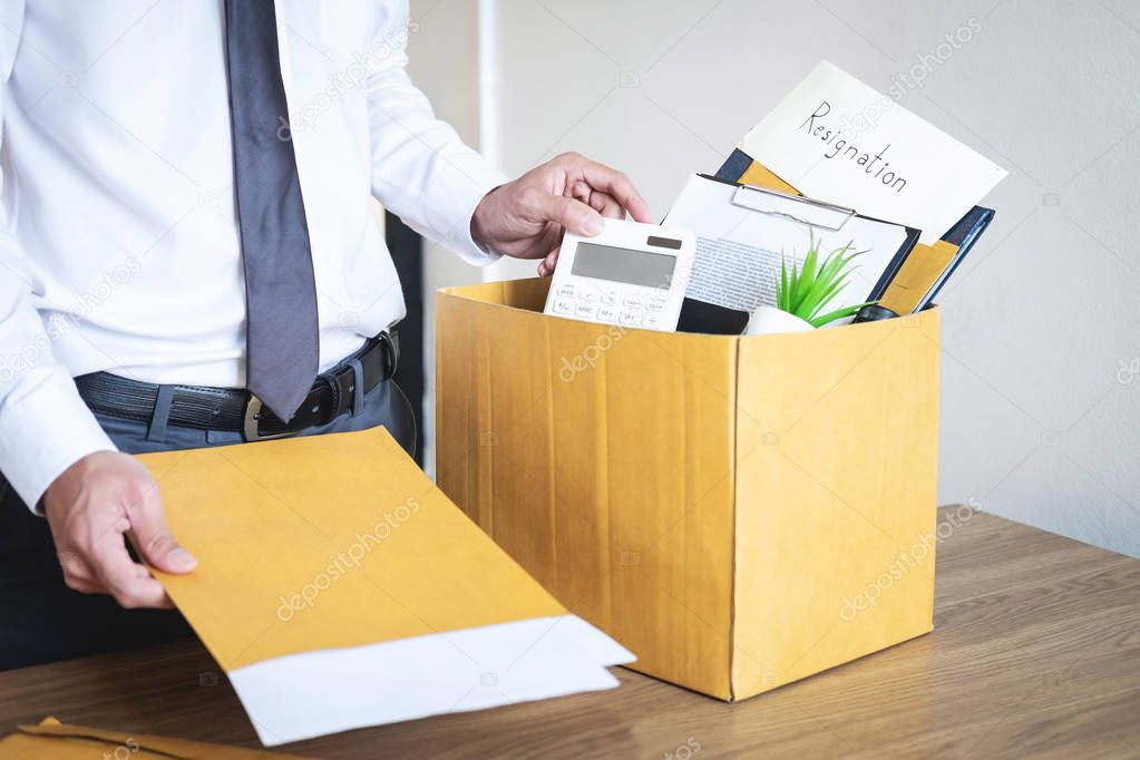 Businessman sending letter will being resignation and carrying packing belongings company and files into brown cardboard box, changing and resigning from work concept.