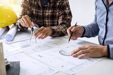 İnşaat mühendisi veya mimar, çalışma sahasındaki mimari projenin çizim ve çizim toplantısına ilişkin bilgileri incelerken bir planı da tartışır..