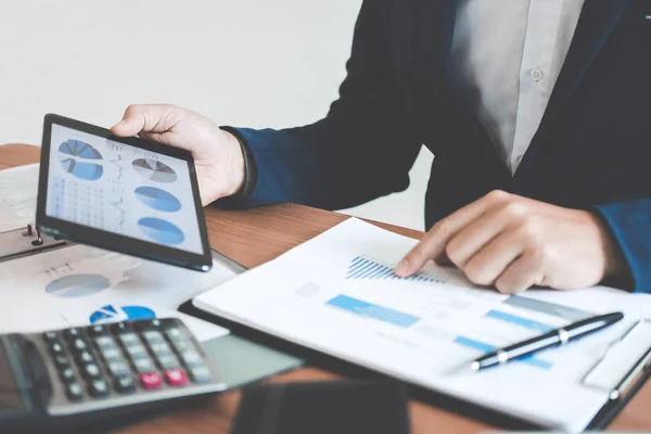 Businessman hands using text information on digital tablet to analyze financial statistical chart data and calculate cost of investment project.